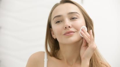 Una chica aplicándose exfoliante frente al espejo.