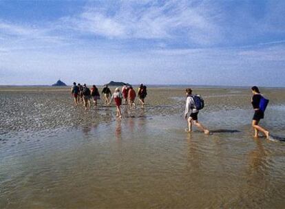 Excursionistas caminan durante la marea baja hacia el monte Saint Michel (izquierda), que se eleva en esta bahía de Normandía (Francia) junto a la isla de Tombelaine.