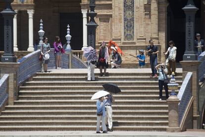 Un grupo de turistas se protege del sol con sombrillas y pañuelos en la Plaza de España de Sevilla.