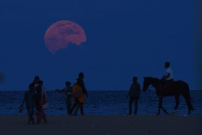 Un home a cavall entre la gent que mira la lluna sobre la platja de Chennai (Índia).