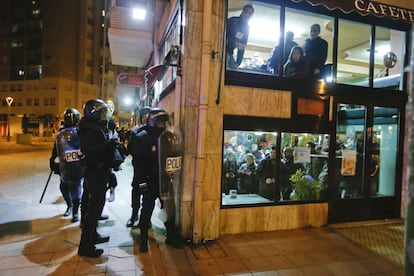 Un grupo de policías se dispone a doblar una esquina ante la atenta mirada de los clientes de una cafetería.
