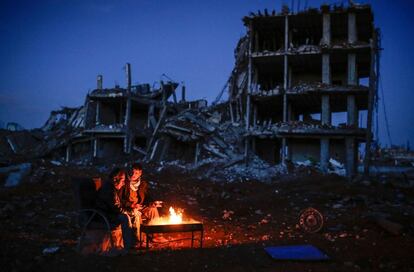 Dois curdos sentados ao redor de uma fogueira próximo a um edifício destruído na cidade de Kobane, na Síria.