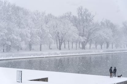 Una pareja pasea a su perro cerca del Monumento a Lincoln mientras cae la nieve, en Washington.