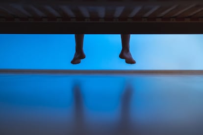 Una persona sentada en una cama con los pies colgando.