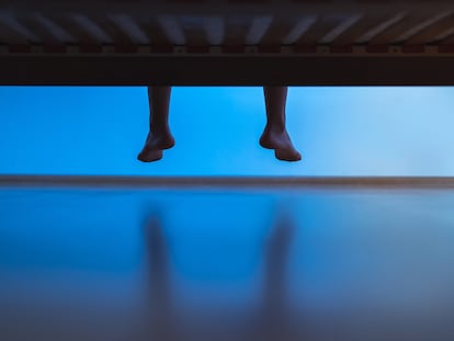Una persona sentada en una cama con los pies colgando.