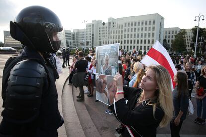 Una mujer muestra a un antidisturbios enmascarado un cartel con fotografías de una joven herida por la policía durante las protestas,  este sábado en Minsk.