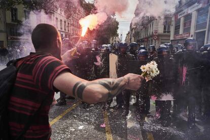 Un hombre sostiene un ramo de flores y una antorcha mientras se enfrenta a la policía antidisturbios durante una manifestación contra la reforma laboral prevista del gobierno, en Lyon, Francia.