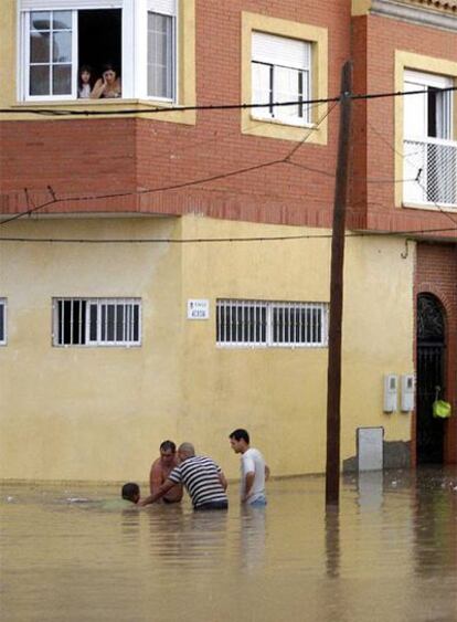 Vecinos de Almería intentaban ayer abrir una alcantarilla para desaguar la calle.