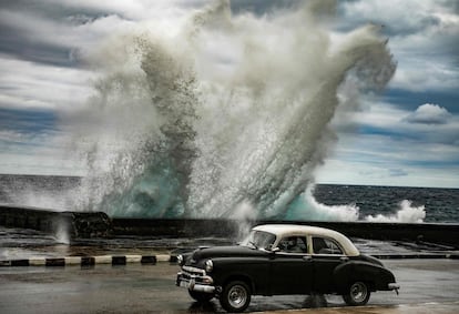 Uno de los míticos 'almendrones', los desvencijados automóviles estadounidenses de los años cincuenta que aun circulan por La Habana, atraviesa El Malecón mientras una ola de gran tamaño impacta contra el muro por los fuertes vientos que azotan estos dias la capital cubana.