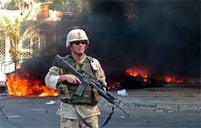 Un soldado estadounidense patrulla delante de las llamas del vehículo militar norteamericano atacado ayer en Bagdad.