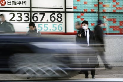 Un hombre mira el móvil delante de un monitor con información de la bolsa en Tokio. 