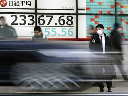 Un hombre mira el móvil delante de un monitor con información de la bolsa en Tokio. 