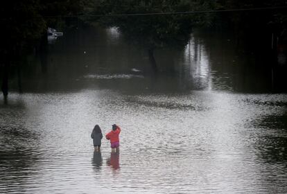 Pessoas caminham por uma estrada alagada neste domingo em Houston.