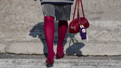 Mujer llevando un muñeco labubu colgado en su bolso rojo.