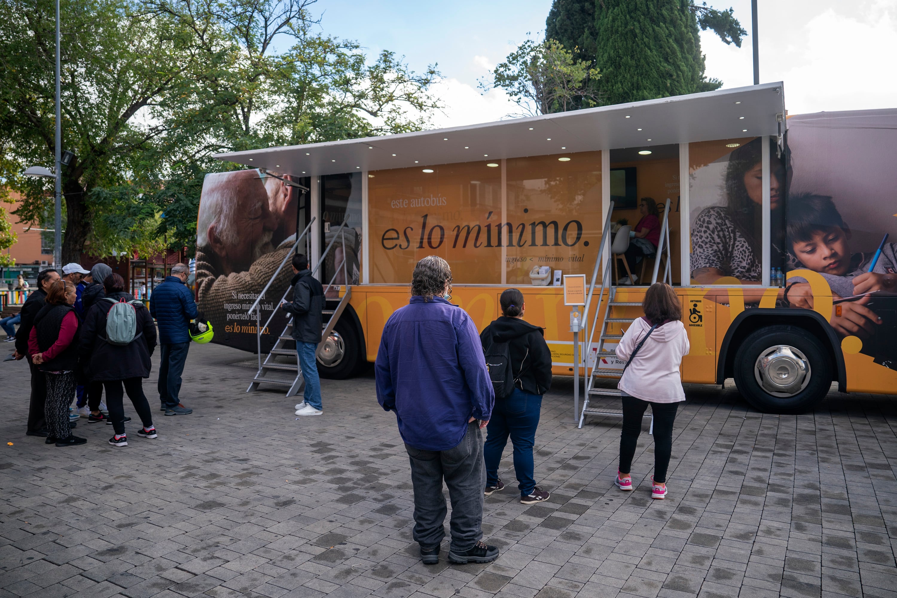 Gente esperando para entrar en un autobús que informa sobre el Ingreso Mínimo Vital (IMV) en Parla (Madrid), en octubre de 2022.