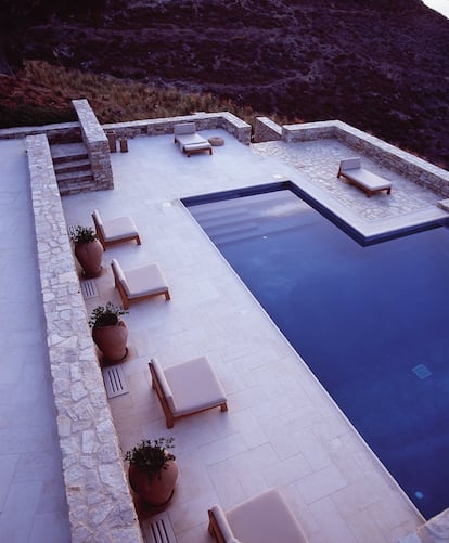 La piscina está rodeada de ánforas en las que plantaron hierbas aromáticas.En el terreno que rodea la casa sembraron mirto y romero. Las butacas de Gijs de Piet Boon amueblan también esa zona. <br> Es difícil saber si esta vivienda en Antíparos, una de las islas Cícladas menos desarrolladas (“aquí los burros no han sido sustituidos por las motos”, apunta la dueña californiana), fue construida más como refugio o como escaparate. De una parte, los arquitectos Tala Mikdashi y Maria Doxa la diseñaron parcialmente excavada en el terreno para disimular la doble altura de la zona de dormitorios. También la forraron de piedra local. Con ese camuflaje buscan no perturbar el paisaje y al mismo tiempo facilitar la conservación de la vivienda, sometida al viento meltemi, seco y portador de polvo y arena. De otra parte, la piscina y el porche sobre un bancal forman un innegable escaparate social: un hogar grande para celebrar y convivir. Sin embargo, es el confort y la naturalidad lo que marca el interiorismo de la griega Marilena Rizou. La vegetación responde al clima seco: olivos, romero y un cedro centenario que —junto a las vistas— determinó la posición de la casa en el terreno. El resto es sencillo y atemporal: tonos neutros, mucha madera maciza —de roble y de iroko— y un mobiliario cuidado pero austero. Ninguna decoración podría competir con el paisaje. 