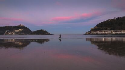 Dos personas corren al amanecer por la orilla de la playa de La Concha de San Sebastián, donde hoy el cielo despejado y el viento del sur elevarán la temperatura máxima a 17ºC.