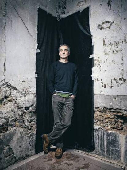 Olivier Assayas posa apoyado en una pared que es como nuestra enferma sociedad: algo roto con un fondo muy negro.
