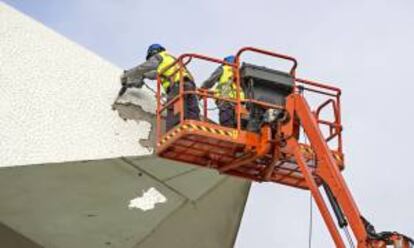 Dos operarios trabajan, desde una plataforma elevadora, en la retirada del revestimiento de la cubierta del Palau de les Arts tras los deprendimientos del pasado mes de diciembre.