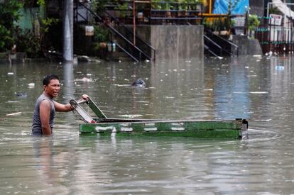 Un hombre empuja un carro de madera por una calle inundada por las lluvias del monzón en Quezon (Filipinas).