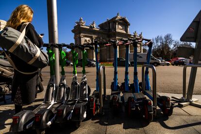 Una mujer consulta su móvil junto a patinetes eléctricos de las empresas Lime y Dott, en la Puerta de Alcalá, en Madrid. SAMUEL SÁNCHEZ