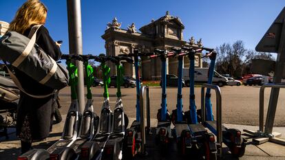 Una mujer consulta su móvil junto a patinetes eléctricos de las empresas Lime y Dott, en la Puerta de Alcalá, en Madrid. SAMUEL SÁNCHEZ