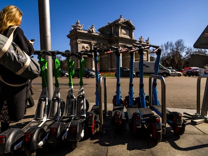 Una mujer consulta su móvil junto a patinetes eléctricos de las empresas Lime y Dott, en la Puerta de Alcalá, en Madrid. SAMUEL SÁNCHEZ