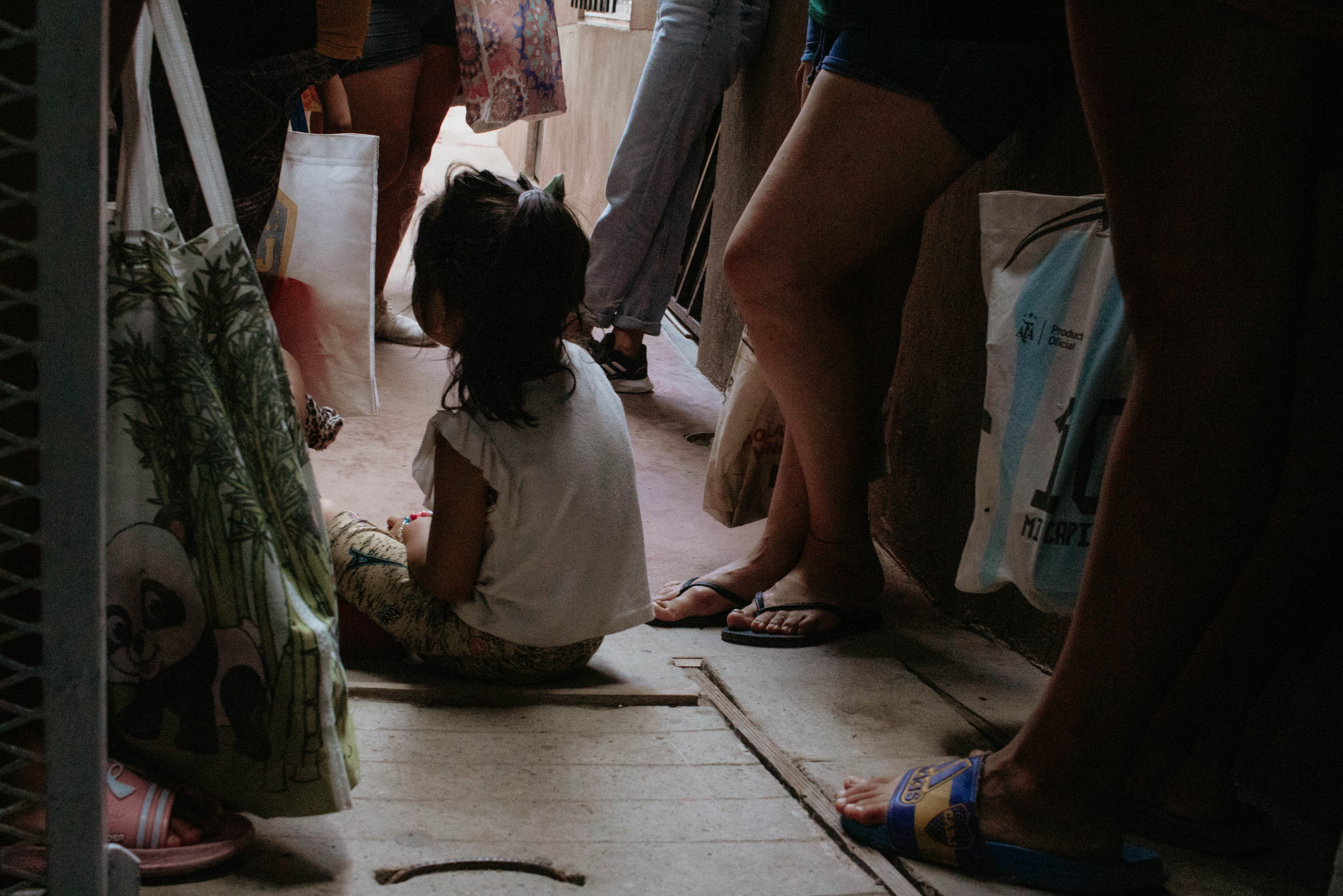 Una niña espera sentada junto a la cola para recibir comida.