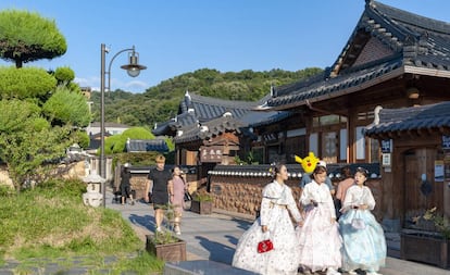 Turistas vestidas con el tradicional 'hanboknam' pasan ante uno de los 'hanoks' de aldea de Jeonju, en Corea del Sur.