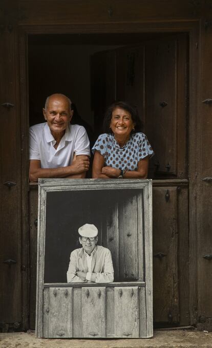 Juan y Elisa Delibes posan en la puerta de la Casona de Sedano con un retrato de Miguel Delibes en la misma posición y mismo lugar; en el décimo aniversario de su fallecimiento.