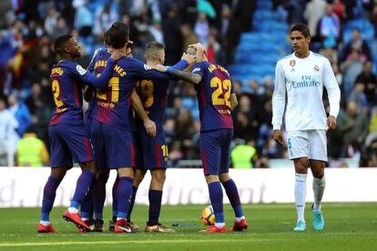 El defensa del FC Barcelona Alex Vidal celebra con sus compañeros tras marcar el tercer gol de su equipo mientras pasa el defensa francés del Real Madrid, Raphael Varane.