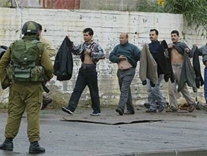 Un grupo de palestinos se levanta la ropa ante la mirada de un soldado israelí en el paso fronterizo de Erez, en la franja de Gaza.