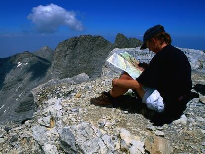 Un montañero descansa en la cima Skolio del monte Olimpo (Grecia), con las cumbres Stefani y Mytikas al fondo.