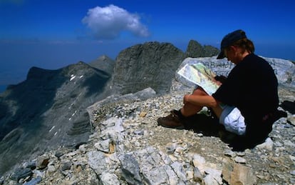 Un montañero descansa en la cima Skolio del monte Olimpo (Grecia), con las cumbres Stefani y Mytikas al fondo.