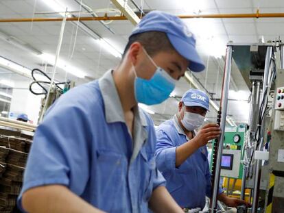 Empleados chinos con mascarilla durante su jornada laboral en una fábrica de la empresa de componentes SMC.