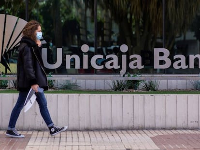 Una mujer pasea ante la sede de Unicaja en Málaga.