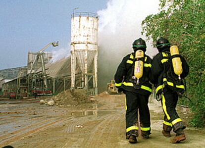 Dos bomberos se acercan al silo de la empresa Fertiberia, donde se produjo la nube contaminante.