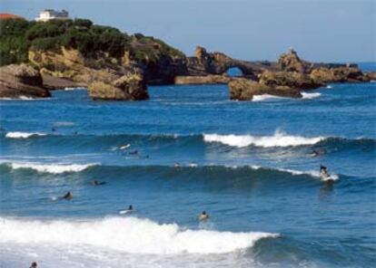 Surfistas disfrutan de las olas de Biarritz. Al fondo, la Roca de la Virgen, un paseo costero muy concurrido.