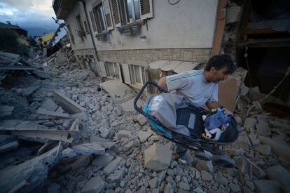 Un hombre transporta un carrito de bebé por encima de los escombros, tras el terremoto de Amatrice.