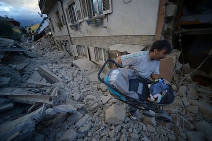 Un hombre transporta un carrito de bebé por encima de los escombros, tras el terremoto de Amatrice.