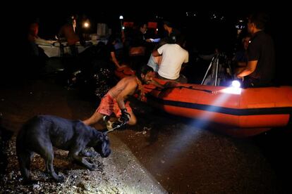 Un hombre, junto a su perro, empuja un bote salvavidas durante la evacuación de vecinos en el pueblo costero de Mati (Grecia).