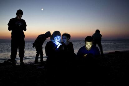 Inmigrantes recién llegados a un playa de la isla griega de Kos miran sus móviles después de haber cruzado en un bote hinchable parte del mar Egeo entre Turquía y Grecia.