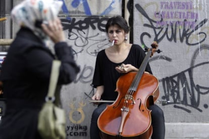 Una mujer con pañuelo islámico pasa ante una joven que toca el violonchelo en una calle de Estambul.