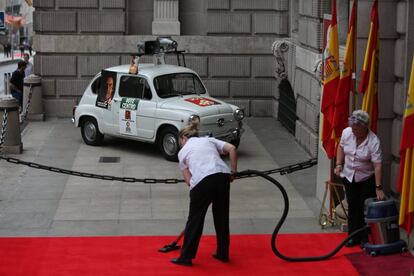 Dos trabajadores limpian la alfombra roja junto a un coche decorado con los carteles electorales de 1977.