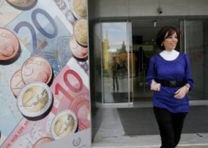 Una mujer camina junto a una valla publicitaria con monedas y billetes de euro. EFE/Archivo