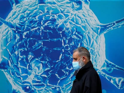 Un hombre con mascarilla pasa junto a un cartel que representa un coronavirus en Oldham, Reino Unido en agosto de 2020.