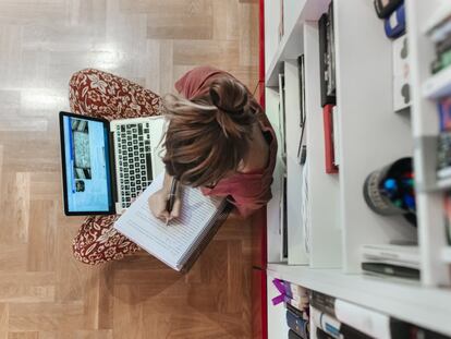 Una mujer escribe a mano mientras consulta su ordenador.