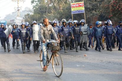 Un hombre montado en bicicleta pasa por delante del cordón policial encargado de reprimir las protestas de los trabajadores de la industria textil en Ashulia, en las afueras de Dhaka (Bangladesh).