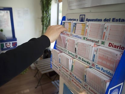 Un hombre coge una quiniela de fútbol del expositor de una administración de loterías de Sevilla.