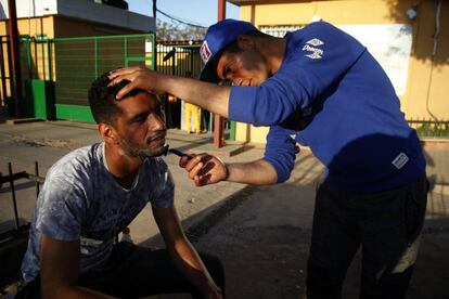 Un refugiado sirio afeita a un compa&ntilde;ero en las puertas del CETI de Melilla.